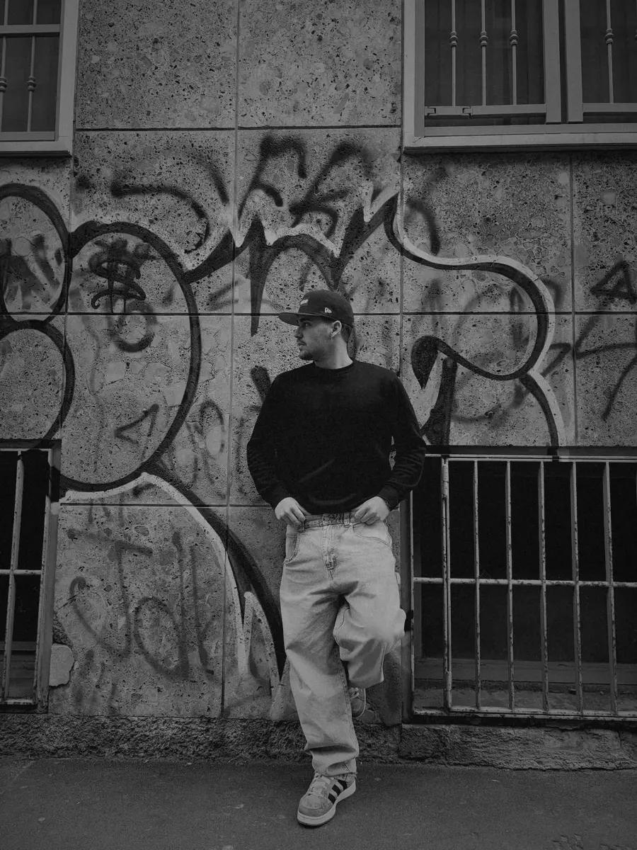 Black and white photo of Valentín leaning on a graffiti wall.