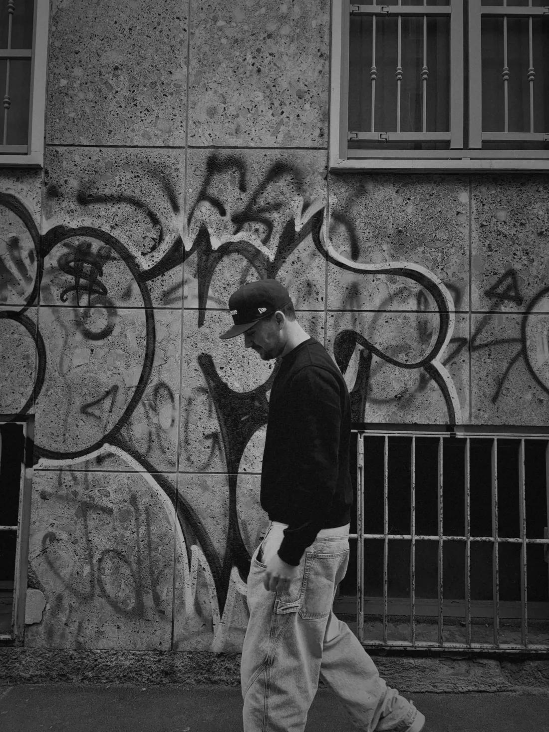 Black and white photo of Valentín walking past a graffiti wall.