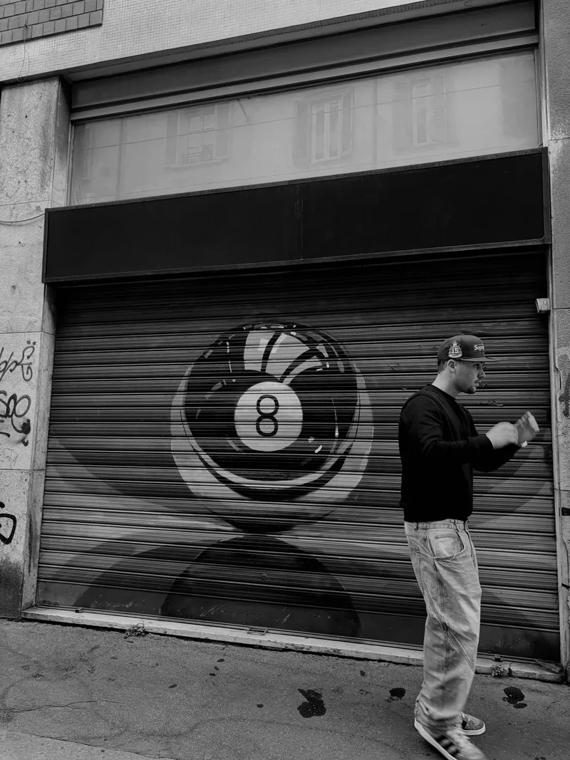 Black and white photo of Valentín in front of a shutter painted with a big 8-ball.